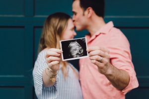 Man and woman in front of a house door holding an ultrasound photo.