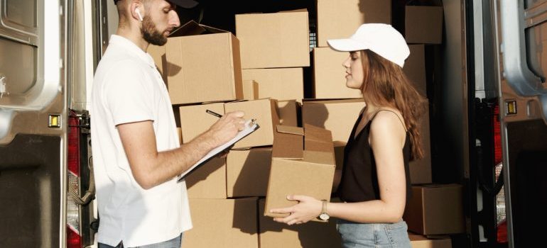 A woman talking to a mover near a van with boxes.