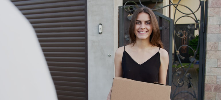 A woman holding a cardboard box in front of a house, before hiring the best long distance movers Miami Beach FL offers.