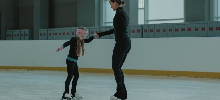 A woman teaches a young girl to skate in an ice arena 
