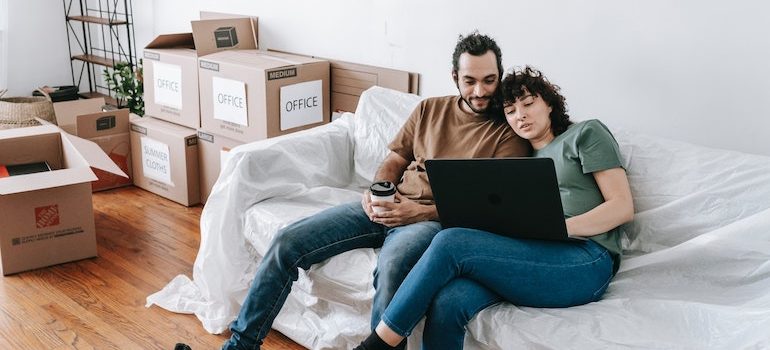 man and woman on a sofa surrounded by boxes looking at computer 