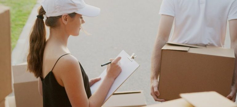 a woman taking notes while a man is carrying a box to load it into the truck