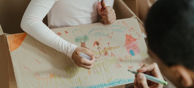 Kid drawing with a parent on a cardboard box.