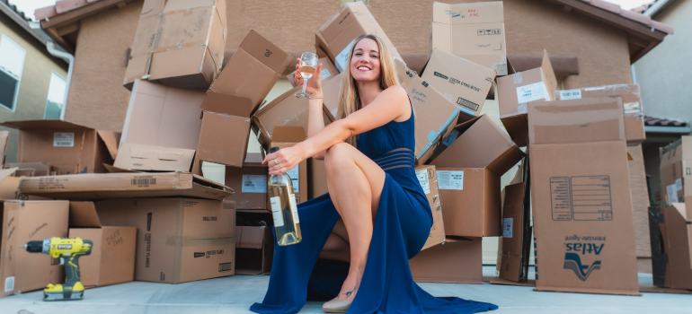 a woman drinking champaigne in front of cardboard boxes that are in her driveway
