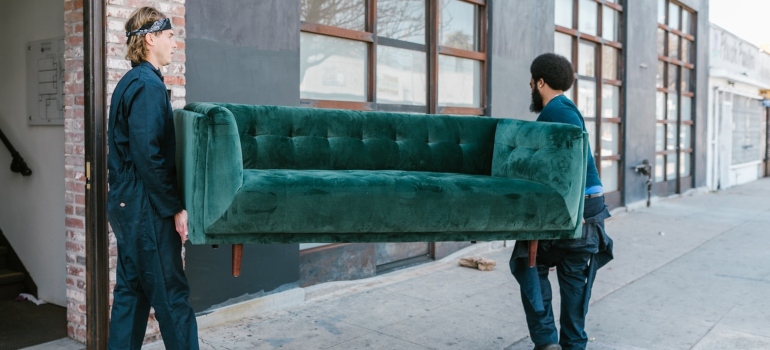 two movers carrying a green couch over a street