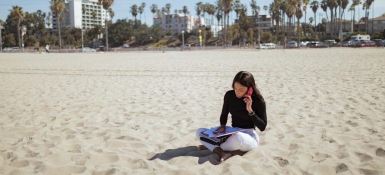 Girl sitting on the sand at the beach with telephone and working